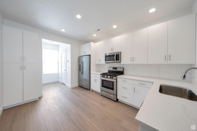 kitchen with a sink, stainless steel appliances, light wood-style flooring, backsplash, and light countertops
