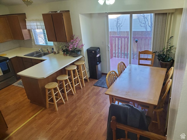 kitchen featuring light wood-style flooring, a breakfast bar, a sink, range with electric cooktop, and light countertops