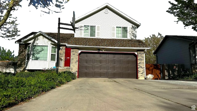 split level home featuring fence, concrete driveway, a garage, and brick siding