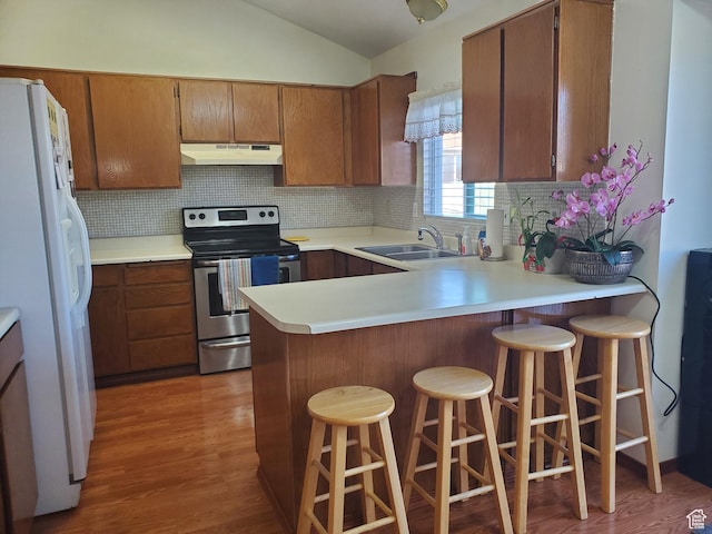 kitchen featuring white fridge with ice dispenser, under cabinet range hood, a sink, stainless steel range with electric cooktop, and vaulted ceiling
