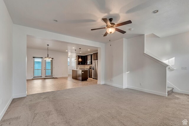 unfurnished living room featuring a ceiling fan, stairs, light carpet, and baseboards