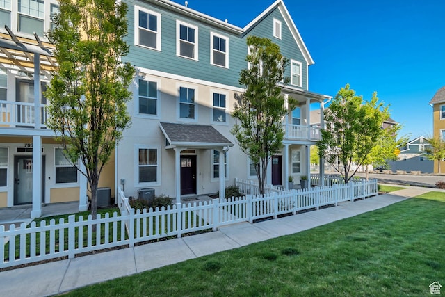 view of front of property featuring a fenced front yard, stucco siding, a front lawn, and central AC unit