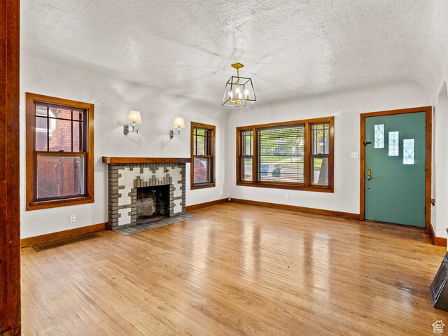 1362 Marilyn Dr, Ogden, UT 84403 - unfurnished living room with light wood-style flooring, a textured ceiling, baseboards, a chandelier, and a brick fireplace