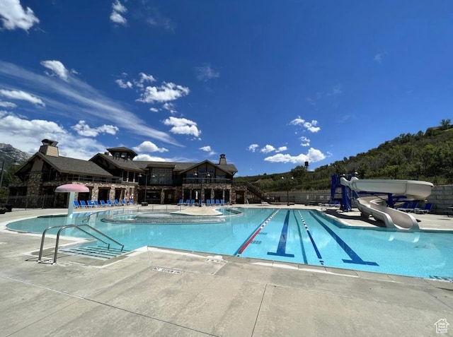 community pool featuring a water slide, fence, and a patio area