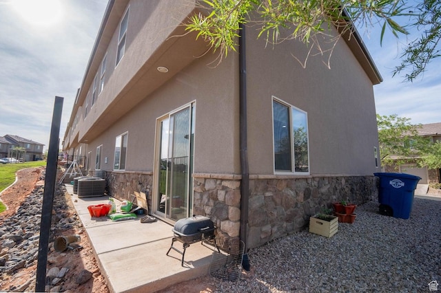 view of side of property with a patio, stucco siding, cooling unit, and stone siding
