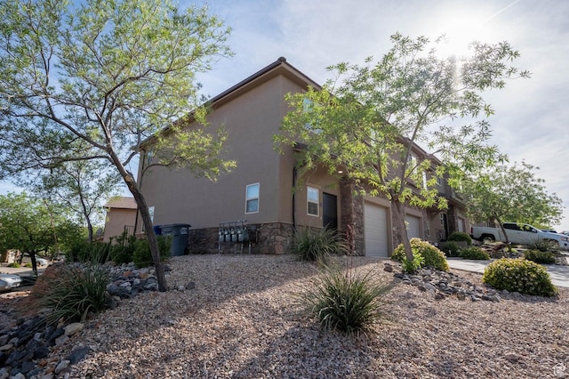 view of home's exterior with stone siding, concrete driveway, stucco siding, and an attached garage