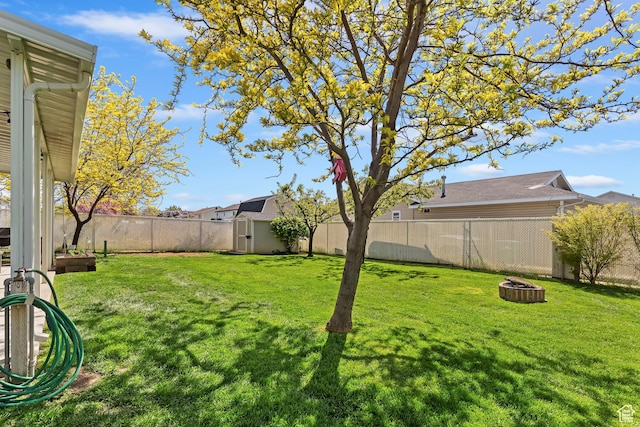 view of yard with an outdoor fire pit, a fenced backyard, an outbuilding, and a storage shed