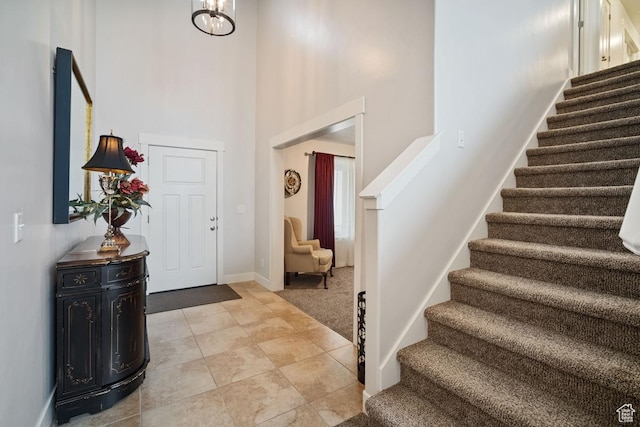 entrance foyer featuring baseboards, light tile patterned flooring, stairs, a chandelier, and a towering ceiling