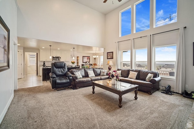 living area with light colored carpet, a ceiling fan, baseboards, and a towering ceiling