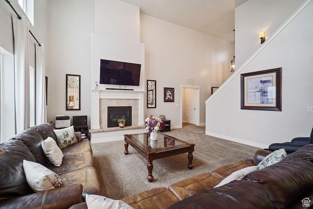 living room featuring baseboards, a glass covered fireplace, stairs, a towering ceiling, and carpet floors