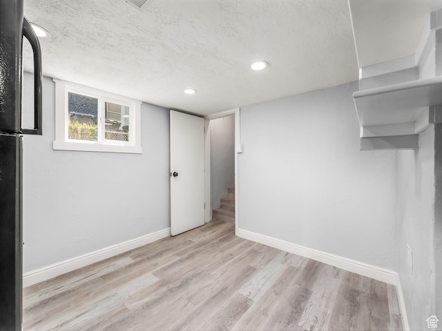 basement with a textured ceiling, baseboards, and light wood-style floors