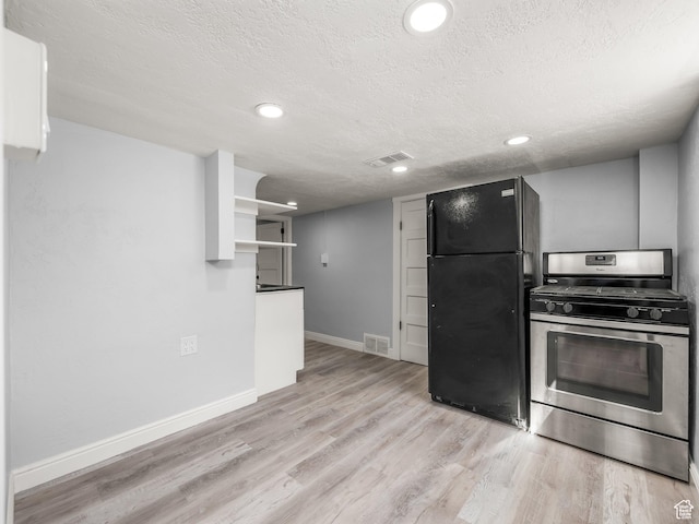 kitchen featuring freestanding refrigerator, gas stove, visible vents, and a textured ceiling