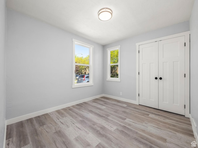 unfurnished bedroom featuring baseboards, light wood-type flooring, and a closet