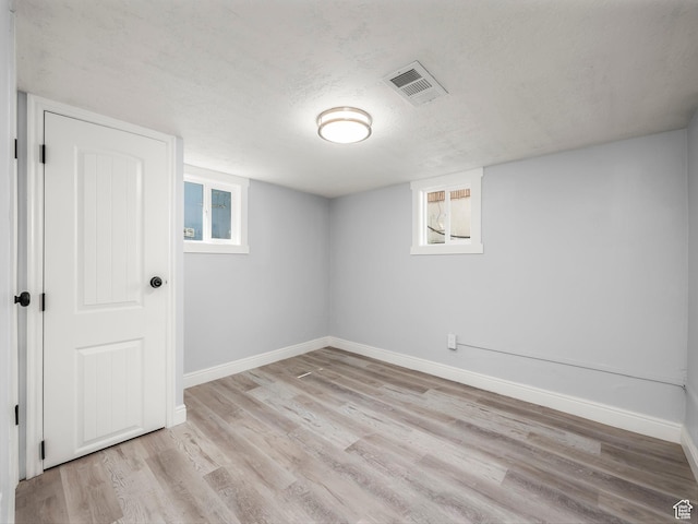 basement featuring baseboards, light wood-style flooring, visible vents, and a textured ceiling