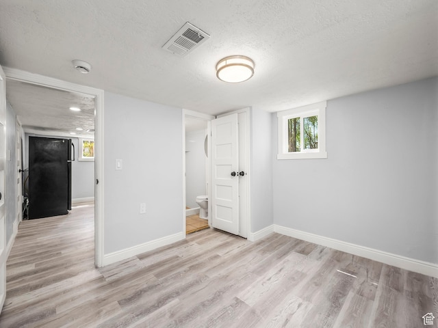 unfurnished bedroom featuring a textured ceiling, baseboards, light wood-type flooring, and visible vents
