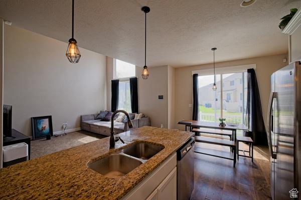 kitchen with a sink, stone countertops, open floor plan, decorative light fixtures, and appliances with stainless steel finishes