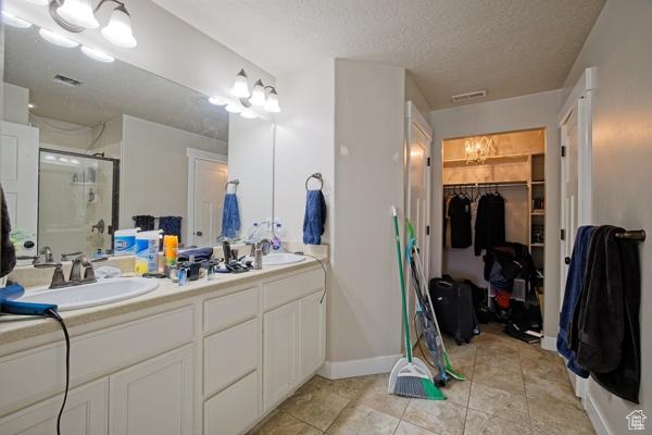 bathroom featuring visible vents, a sink, a shower stall, double vanity, and a walk in closet