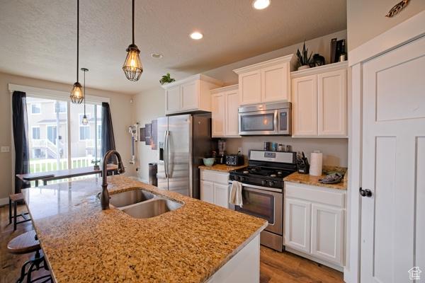 kitchen with a breakfast bar, a sink, stainless steel appliances, a kitchen island with sink, and white cabinetry