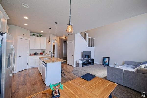 kitchen with a sink, open floor plan, a center island with sink, stainless steel appliances, and white cabinets