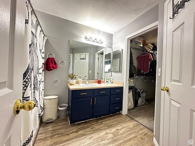 bathroom featuring vanity, a textured ceiling, a spacious closet, and wood finished floors