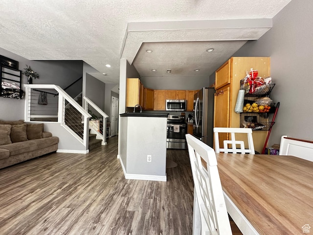 interior space with a textured ceiling, wood finished floors, open floor plan, and appliances with stainless steel finishes