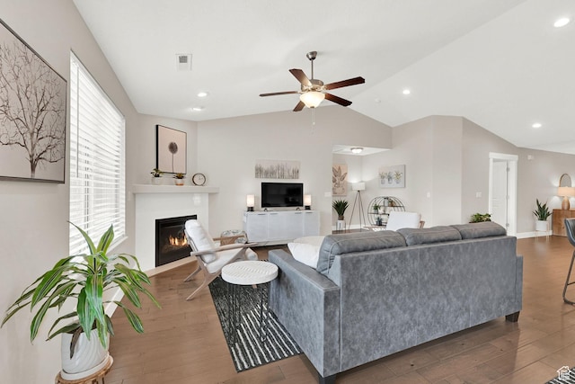 living room with wood finished floors, visible vents, ceiling fan, a glass covered fireplace, and vaulted ceiling