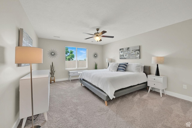 bedroom with a ceiling fan, a textured ceiling, visible vents, baseboards, and light carpet