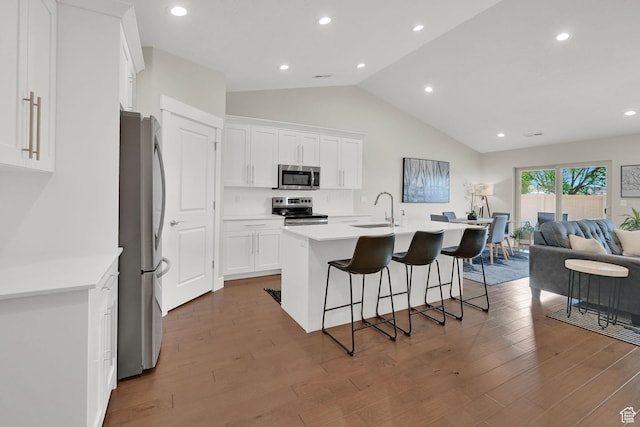 kitchen featuring a breakfast bar, a sink, stainless steel appliances, white cabinets, and a center island with sink