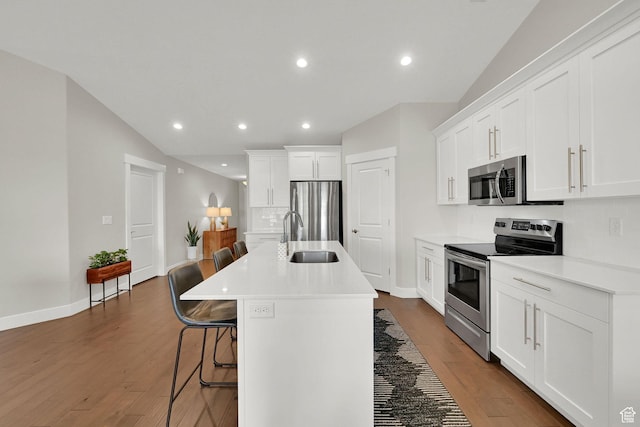 kitchen featuring a breakfast bar, a sink, backsplash, appliances with stainless steel finishes, and dark wood-style floors