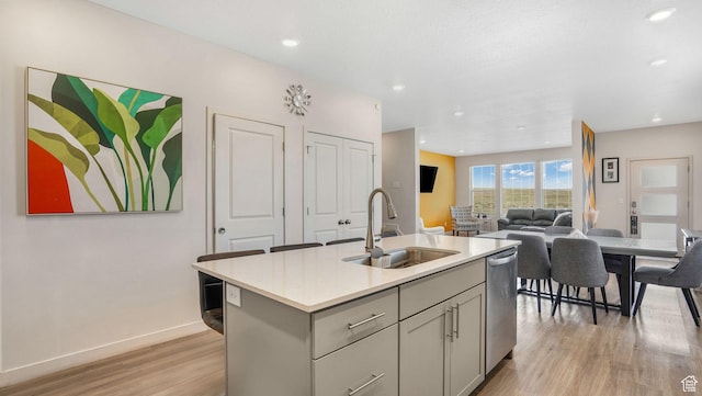 kitchen with light wood-style flooring, gray cabinetry, dishwasher, a sink, and light countertops