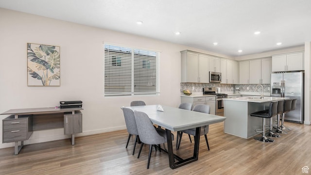 kitchen featuring baseboards, a sink, stainless steel appliances, tasteful backsplash, and light wood-type flooring