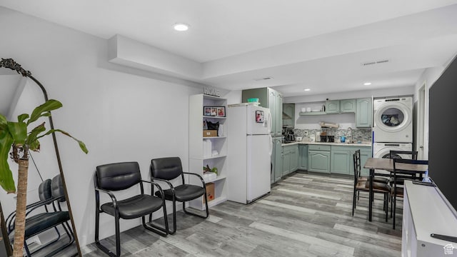 kitchen featuring freestanding refrigerator, green cabinets, visible vents, stacked washer and dryer, and open shelves