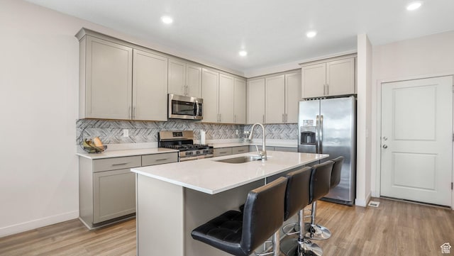 kitchen with a sink, light wood-style floors, stainless steel appliances, tasteful backsplash, and gray cabinets