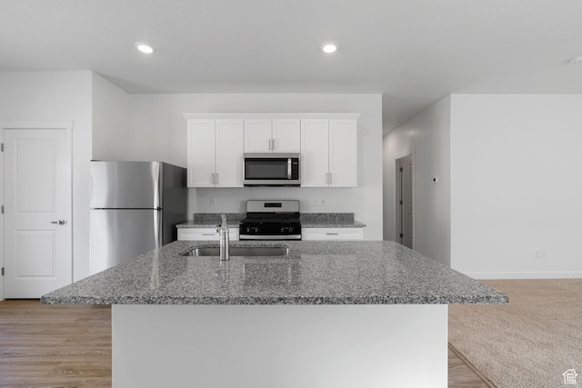kitchen featuring an island with sink, dark stone countertops, a sink, white cabinets, and appliances with stainless steel finishes