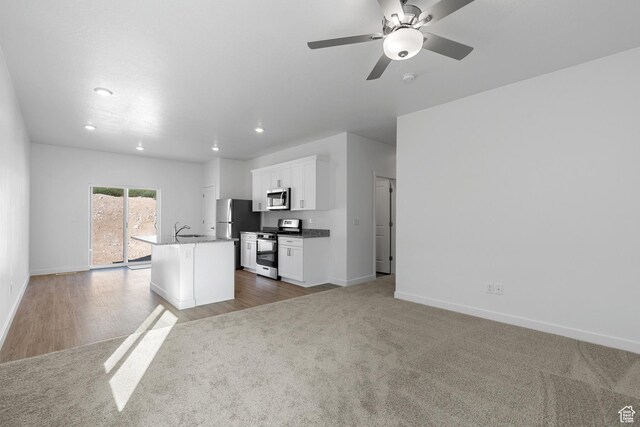 kitchen featuring white cabinets, a center island with sink, baseboards, ceiling fan, and appliances with stainless steel finishes