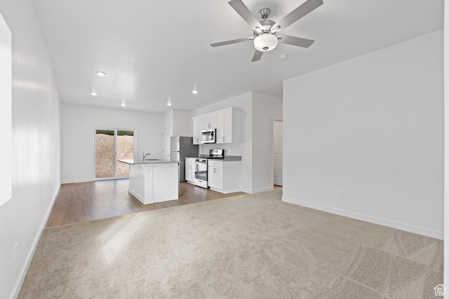 unfurnished living room with recessed lighting, carpet, baseboards, ceiling fan, and a sink