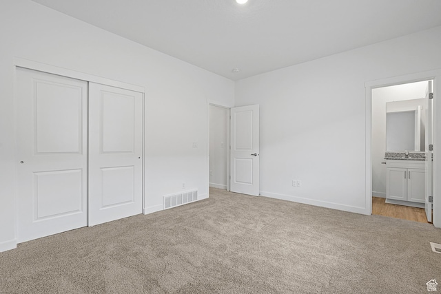 unfurnished bedroom with a closet, ensuite bathroom, visible vents, baseboards, and light colored carpet