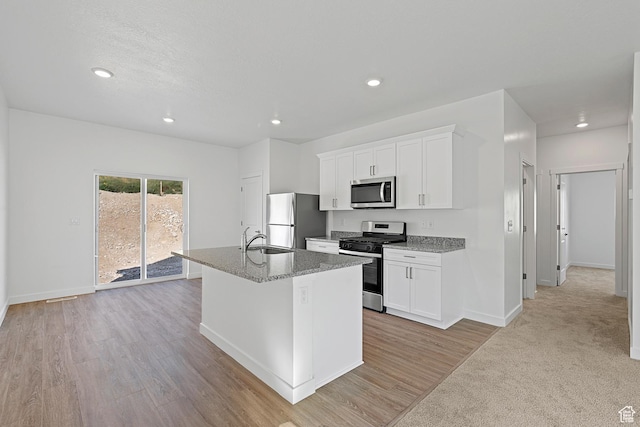 kitchen with a sink, a center island with sink, white cabinetry, baseboards, and appliances with stainless steel finishes