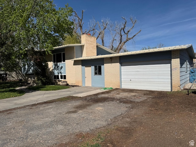 view of front of property with an attached garage, brick siding, a chimney, and aphalt driveway