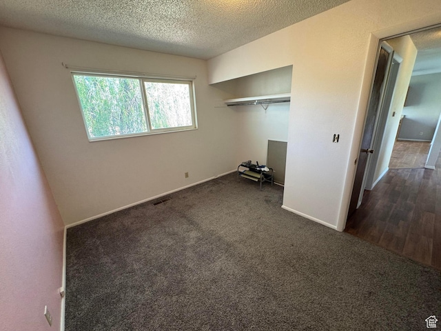 unfurnished bedroom featuring dark colored carpet, baseboards, a textured ceiling, and a closet
