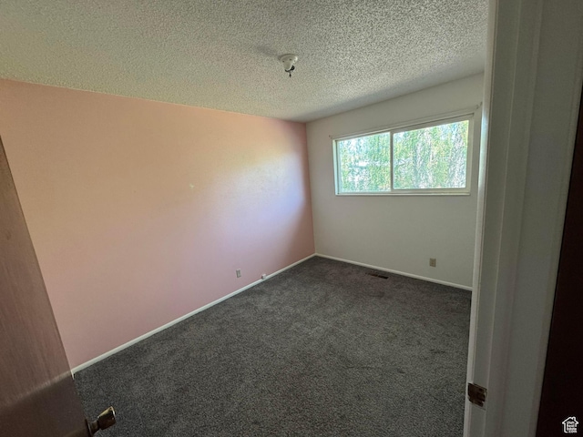 empty room with a textured ceiling, dark colored carpet, and baseboards
