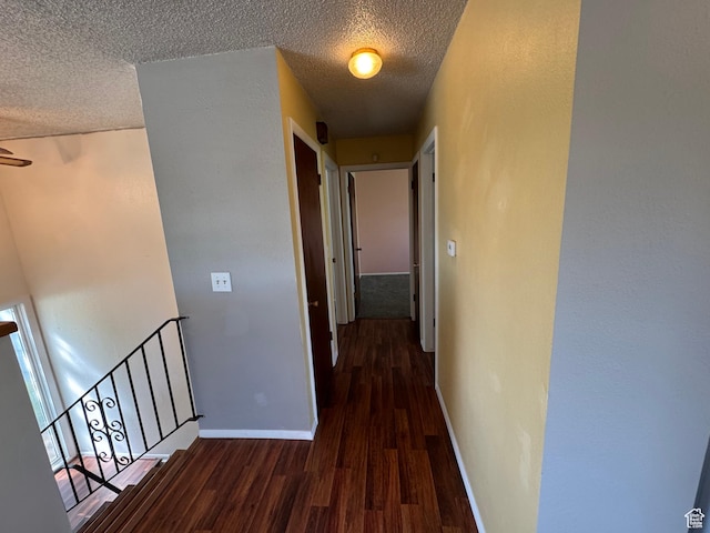 hallway with baseboards, an upstairs landing, a textured ceiling, and wood finished floors