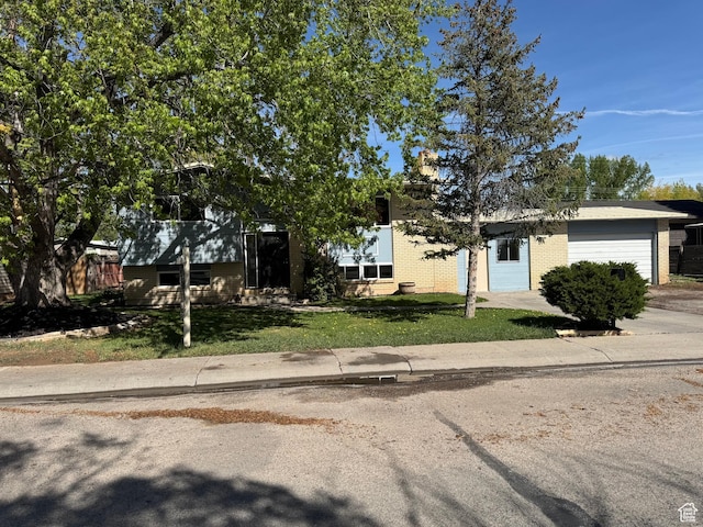 view of property hidden behind natural elements featuring concrete driveway, an attached garage, a front lawn, and brick siding