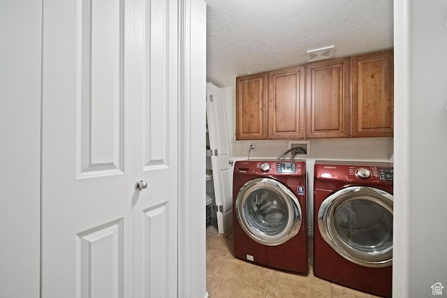 laundry area featuring a textured ceiling, light tile patterned flooring, visible vents, washing machine and clothes dryer, and cabinet space