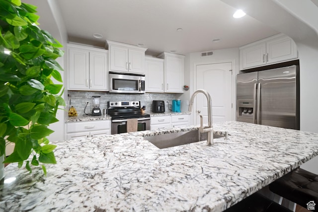 kitchen with tasteful backsplash, visible vents, a sink, stainless steel appliances, and white cabinets