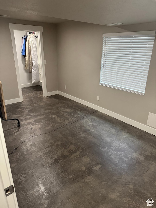 unfurnished bedroom with concrete floors, a closet, baseboards, and a spacious closet