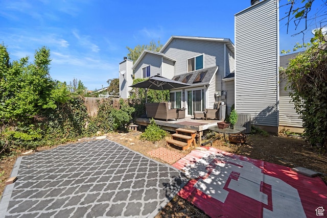 back of property with a deck, a patio area, a chimney, fence, and central AC
