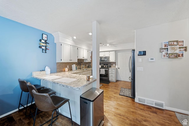 kitchen featuring appliances with stainless steel finishes, a peninsula, a sink, a kitchen breakfast bar, and tasteful backsplash