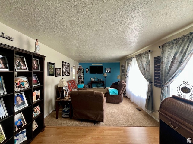 living area featuring carpet floors, visible vents, a textured ceiling, and wood finished floors