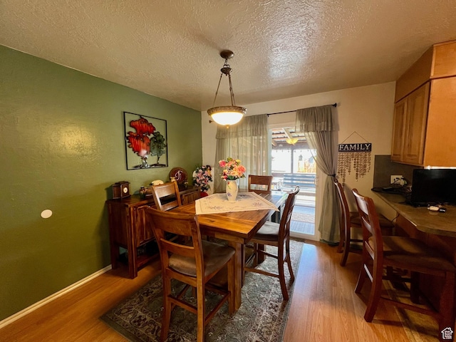 dining space featuring light wood finished floors, a textured ceiling, and baseboards